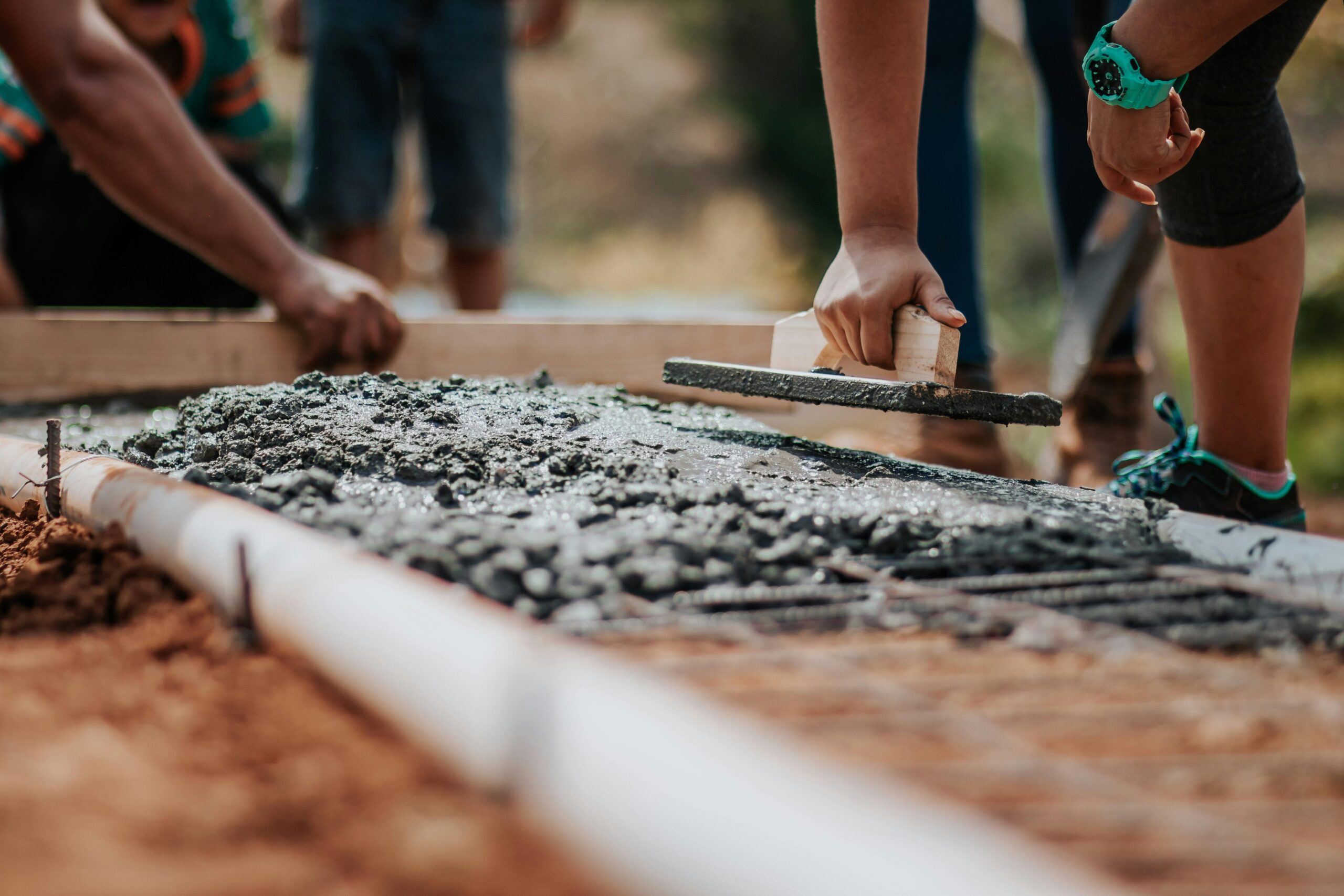 Home Construction workers leveling fresh cement on a sunny day at an outdoor site.